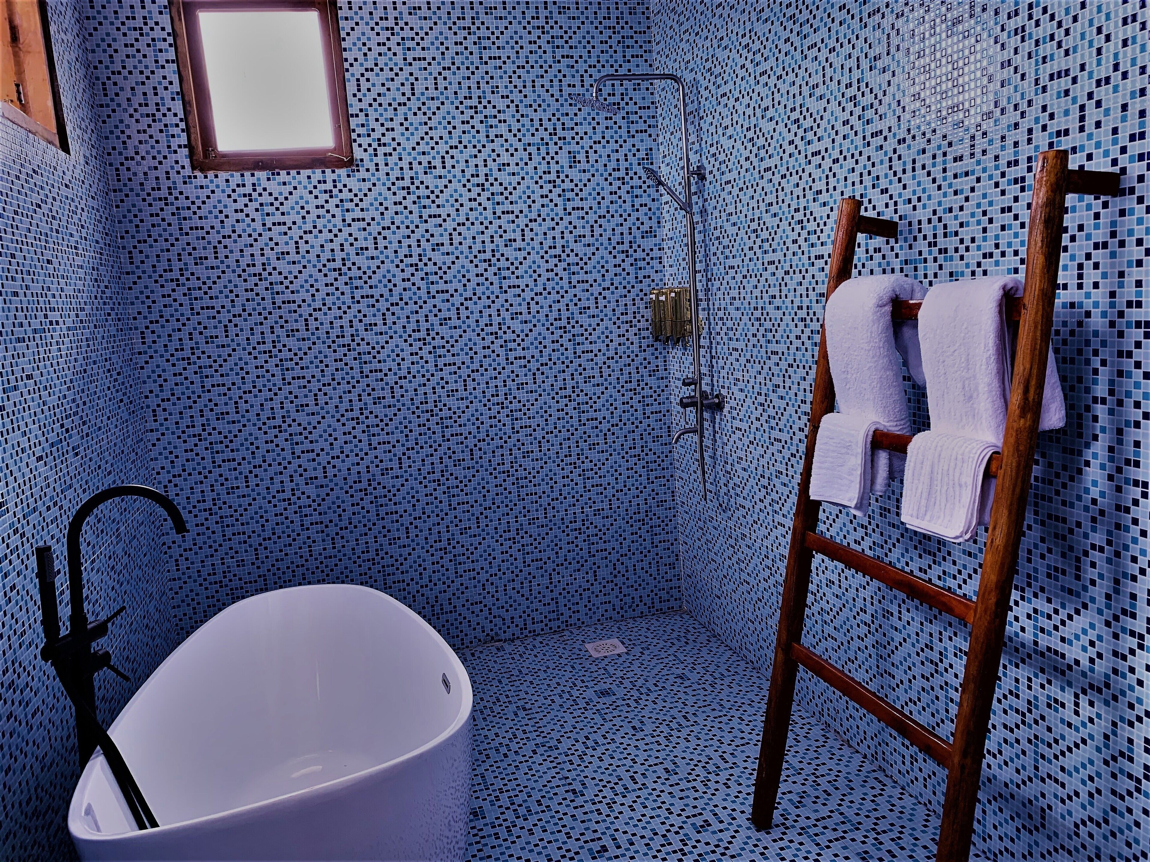 A bathroom with a white bathtub, a wooden ladder, and a shower area with a tiled wall.