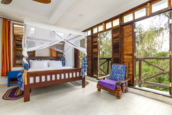 Un dormitorio con una cama con dosel, un banco de madera y ventanas amplias con contraventanas.