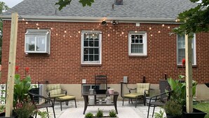 A brick house with a patio area featuring outdoor furniture and potted plants. - Cozy, Convenient, & Comfortable Retreat w/ Firepit, Hammock, Ping Pong, & Coffee (Roanoke)