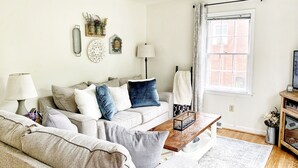 A living room with a sofa, coffee table, and a window with curtains. - Cozy, Convenient, & Comfortable Retreat w/ Firepit, Hammock, Ping Pong, & Coffee (Roanoke)