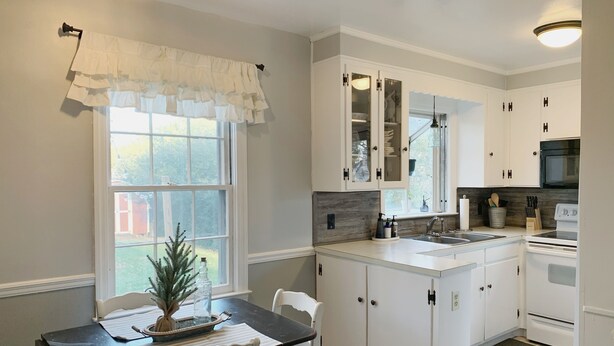 A kitchen with white cabinets, a central island, a dining table with chairs, and a window with a view of greenery. - Cozy, Convenient, & Comfortable Retreat w/ Firepit, Hammock, Ping Pong, & Coffee (Roanoke)