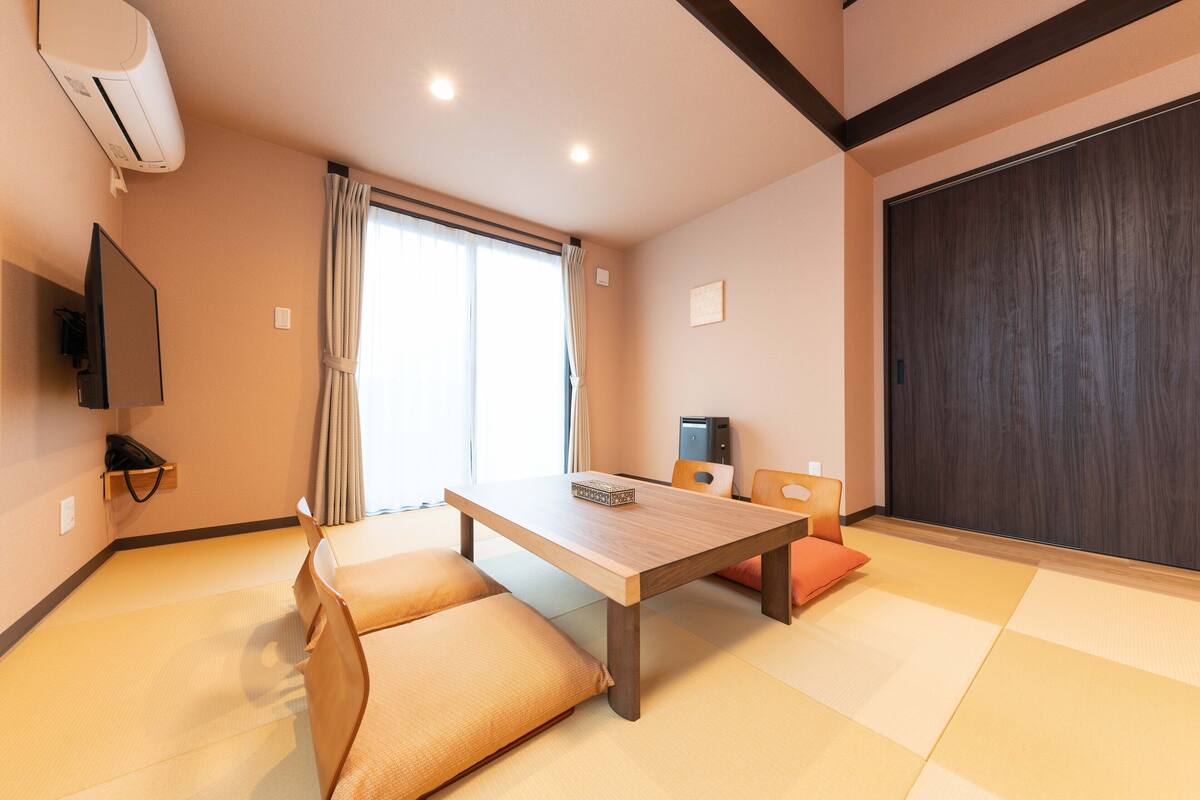 Quarto com tatame, uma mesa de madeira, um sofá, uma televisão e uma porta deslizante.