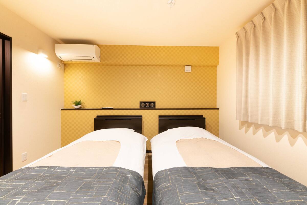 Quarto de hotel com duas camas, uma kitchenette pequena e uma janela com cortinas.