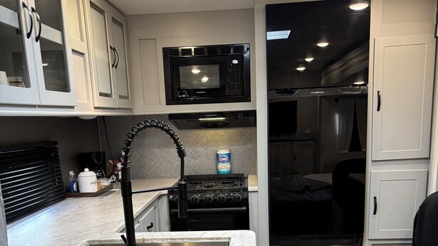 A compact kitchen with white cabinets, a black microwave, a stove, and a sink.