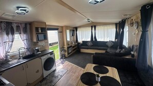 A compact RV interior with a kitchenette, a sofa, and a dining area. - Fluffy Caravan Sleeps 4, Pet-Friendly (Isle of Sheppey)