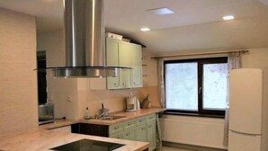 A modern kitchen with a central island, stainless steel range hood, light green cabinets, a window with curtains, and a white refrigerator.
