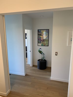 A hallway with a wooden floor, a door leading to another room, and a framed Beatles album cover on the wall.