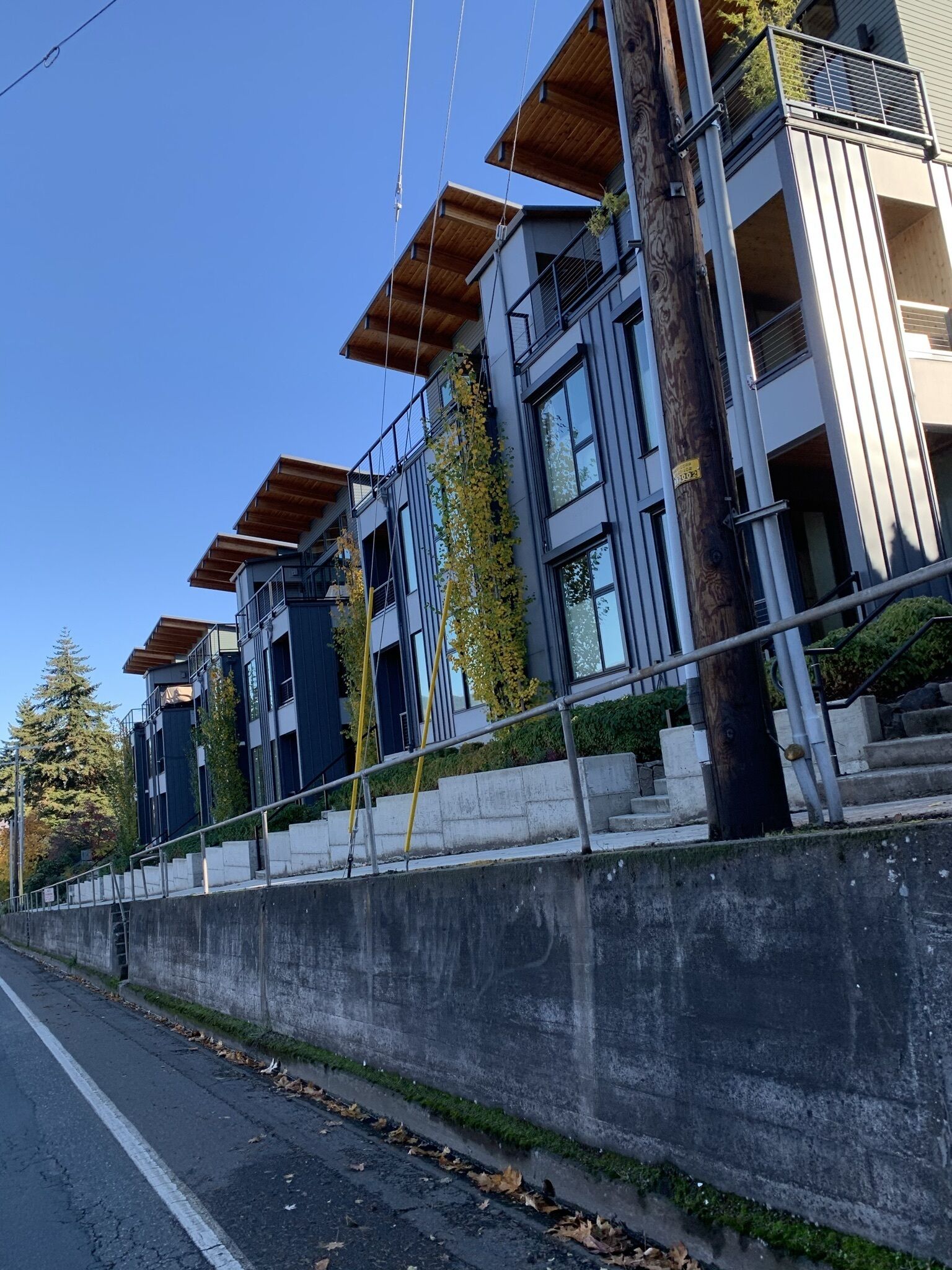 A modern multi-story building with a concrete retaining wall, wooden balconies, and a clear sky.