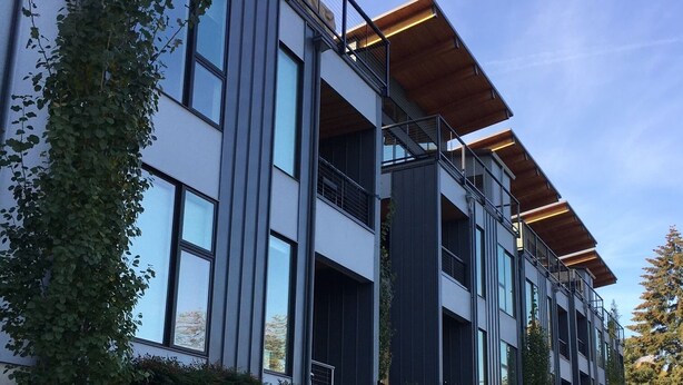 Un edificio moderno de varios pisos con grandes ventanales, un muro de contención de concreto y un sendero.