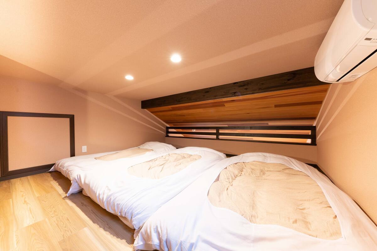 A bedroom with two beds, wooden flooring, a sloped ceiling, and an air conditioning unit.