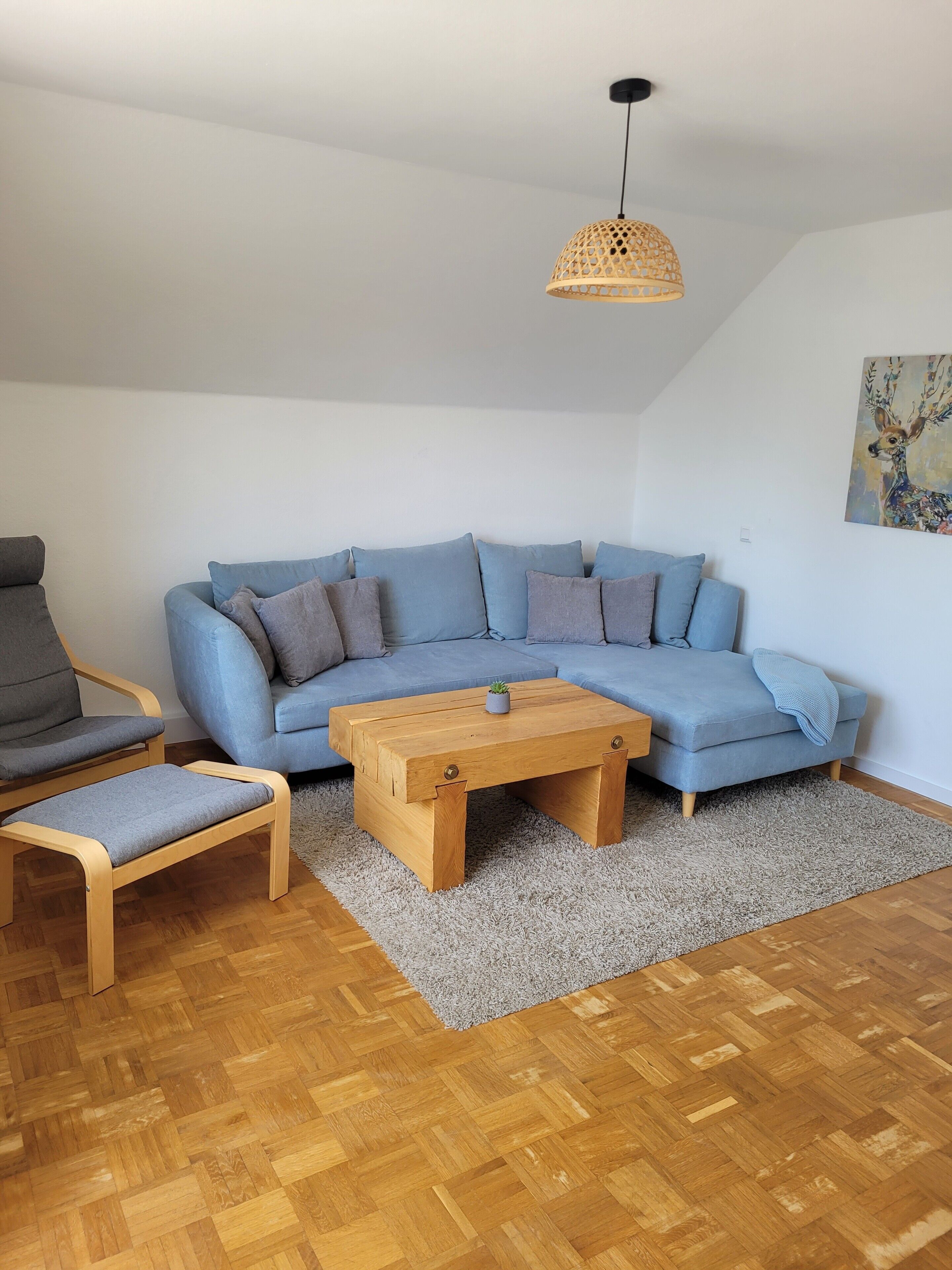 Una sala de estar con un sofá azul, una mesa de centro de madera, un sillón gris y un banco de madera.