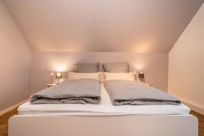 Un lit simple avec deux oreillers, une table de chevet avec une lampe et un luminaire fixé au mur.