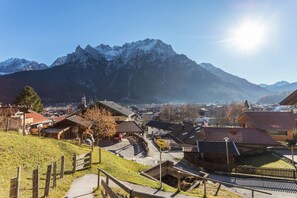 A mountain town with traditional architecture, a paved road, and a clear view of snow-capped mountains.