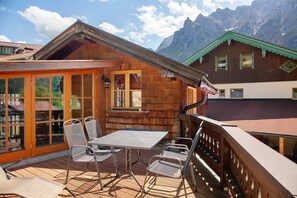 A wooden chalet with a balcony, outdoor seating, and mountain views.