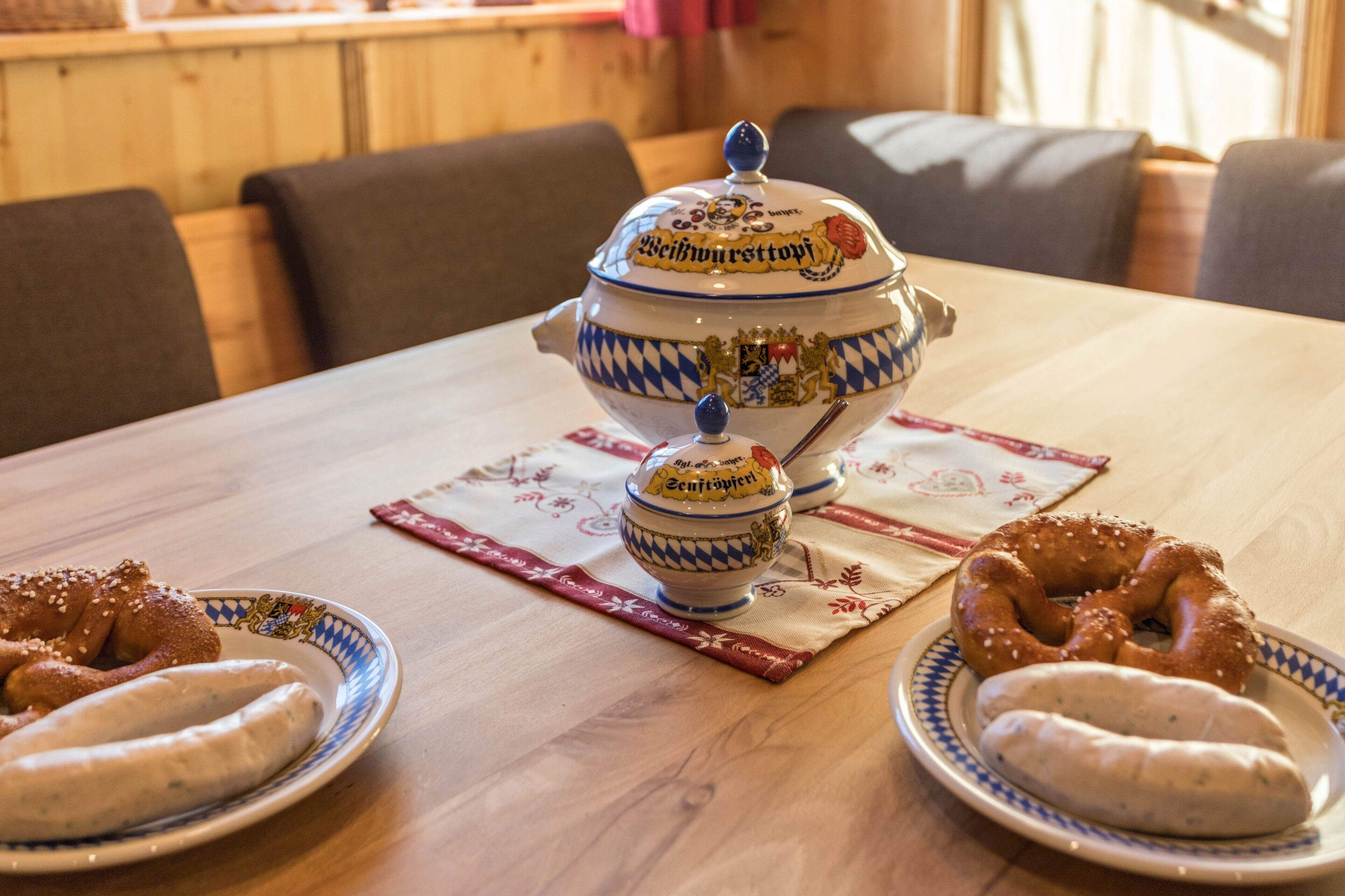 Une table dressée avec un service traditionnel bavarois comprenant un grand saladier, un plus petit saladier et deux assiettes garnies de bretzels et de saucisses.