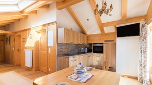 A wooden interior with a dining table, a kitchen with wooden cabinets, and a television mounted on the wall. - Apartment 'Bergkristall' Near the Ski Lift with Mountain View, Wi-Fi & Balcony (Mittenwald)