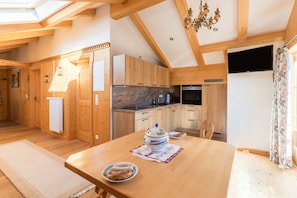 Un intérieur en bois comprenant une table à manger, une cuisine avec des meubles en bois et un téléviseur fixé au mur.