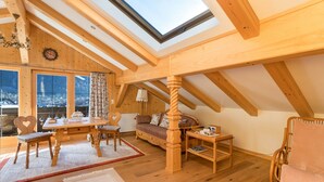 A wooden interior with a skylight, a dining table with chairs, a sofa, and a rocking chair. - Apartment 'Bergkristall' Near the Ski Lift with Mountain View, Wi-Fi & Balcony (Mittenwald)