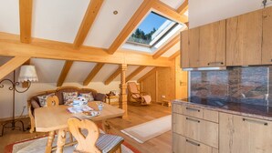 A cozy attic room with a wooden dining table, chairs, a sofa, a rocking chair, a skylight, and a kitchen area with granite countertops. - Apartment 'Bergkristall' Near the Ski Lift with Mountain View, Wi-Fi & Balcony (Mittenwald)