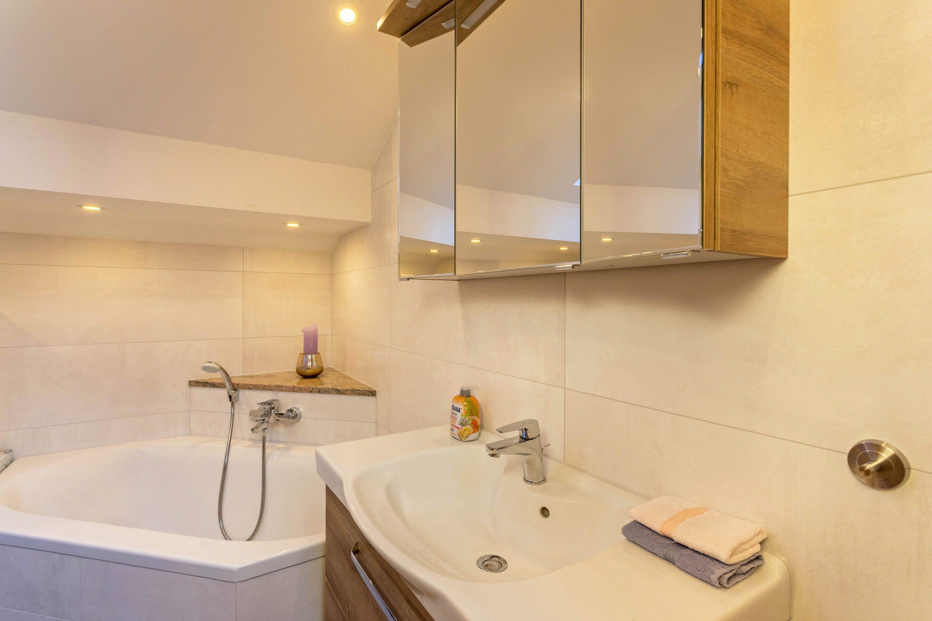 A bathroom with a bathtub, a sink, a mirror, and a shelf with toiletries.