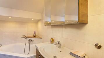 A bathroom with a bathtub, a sink, a mirror, and a shelf with toiletries.