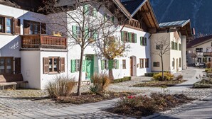 A traditional European building with a cobblestone courtyard, wooden balconies, and a mountain backdrop. - Apartment 'Bergkristall' Near the Ski Lift with Mountain View, Wi-Fi & Balcony (Mittenwald)