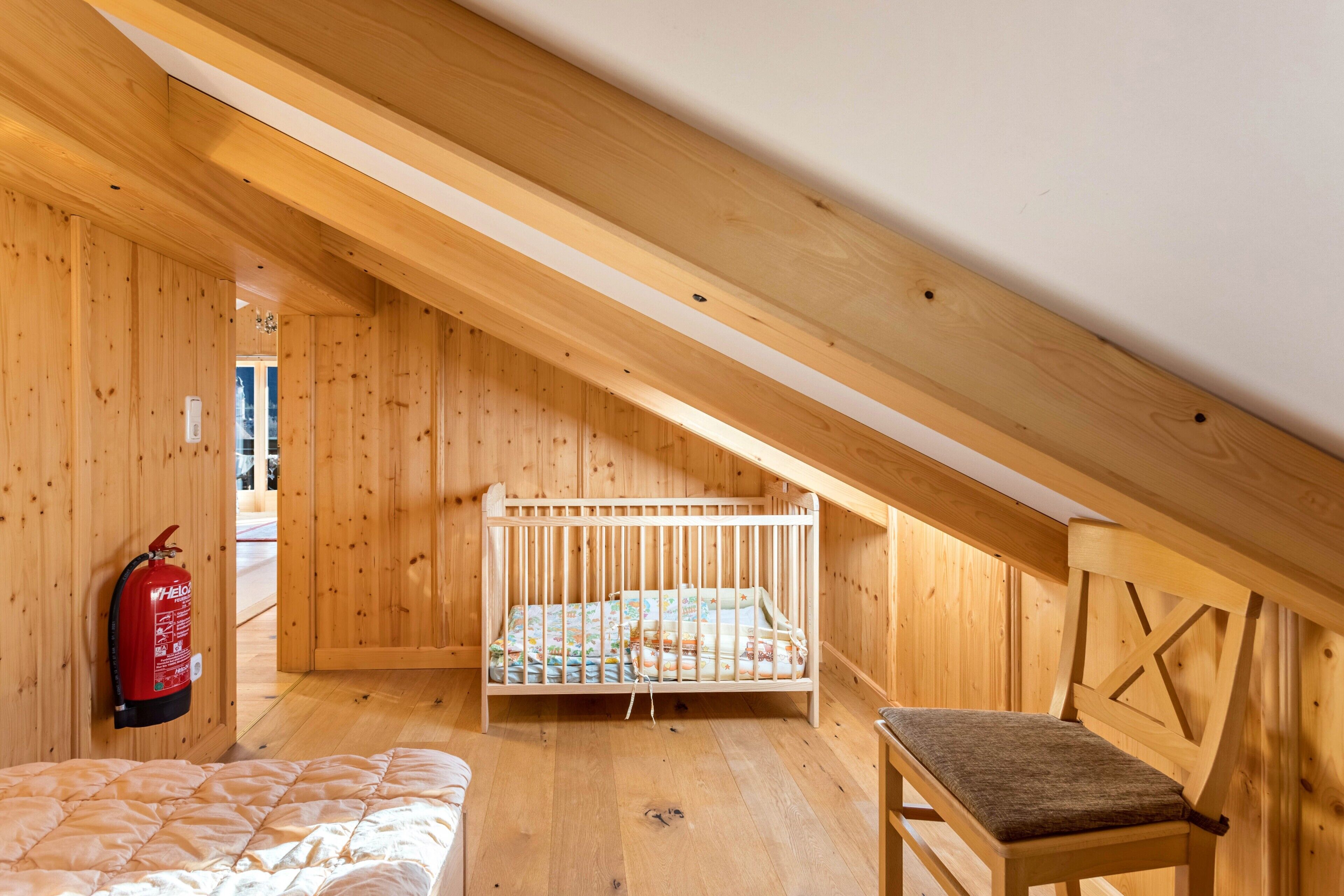 Ein Zimmer mit Holzboden, einem Kinderbett, einem Stuhl und einem Feuerlöscher.