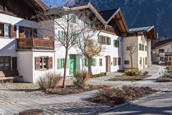 Un bâtiment européen traditionnel, doté d’une cour pavée, de balcons en bois et surplombant un paysage montagneux.