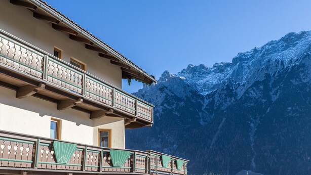 A building with balconies, a mountain backdrop, and a clear sky. - Apartment 'Rosenquarz' Near the Ski Lift with Mountain View, Wi-Fi & Balcony (Mittenwald)