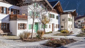 A traditional European building with a cobblestone courtyard, wooden balconies, and a mountain backdrop. - Apartment 'Rosenquarz' Near the Ski Lift with Mountain View, Wi-Fi & Balcony (Mittenwald)