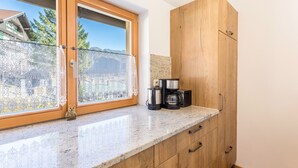 A kitchen with a window, wooden cabinets, and a coffee maker. - Apartment 'Rosenquarz' Near the Ski Lift with Mountain View, Wi-Fi & Balcony (Mittenwald)