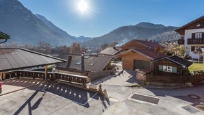 A mountain village with traditional wooden buildings, a parking area, and a clear view of the surrounding mountains. - Apartment 'Rosenquarz' Near the Ski Lift with Mountain View, Wi-Fi & Balcony (Mittenwald)