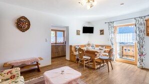 A cozy room with a wooden dining table, chairs, a bench, a television, and a window with curtains. - Apartment 'Rosenquarz' Near the Ski Lift with Mountain View, Wi-Fi & Balcony (Mittenwald)