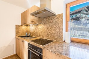 A modern kitchen with granite countertops, stainless steel appliances, and a window with a view of traditional buildings. - Apartment "Bernstein" Near the Ski Lift with Mountain View, Wi-Fi, Balcony & Terrace (Mittenwald)