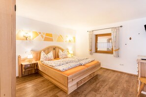 Een slaapkamer met een houten bed, nachtkastjes, een nachtlampje en een raam met gordijnen.