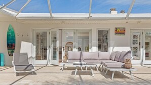 Ein Poolbereich mit weißer Lounge-Möblierung, darunter eine Liege und ein Sofa, in der Nähe einer verglasten Tür.