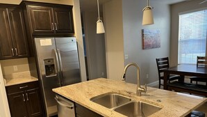A kitchen with dark cabinets, stainless steel appliances, a double sink, and pendant lighting.