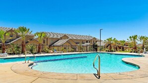 A swimming pool with a curved edge, surrounded by palm trees and lounge chairs.