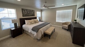 A bedroom with a large bed, bedside tables, a ceiling fan, and a dresser.