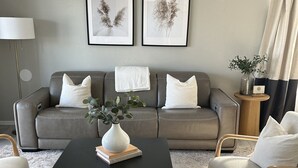 Una sala de estar con un sofá gris, dos cuadros en la pared, una mesa de centro negra con un jarrón y libros, y una alfombra estampada.