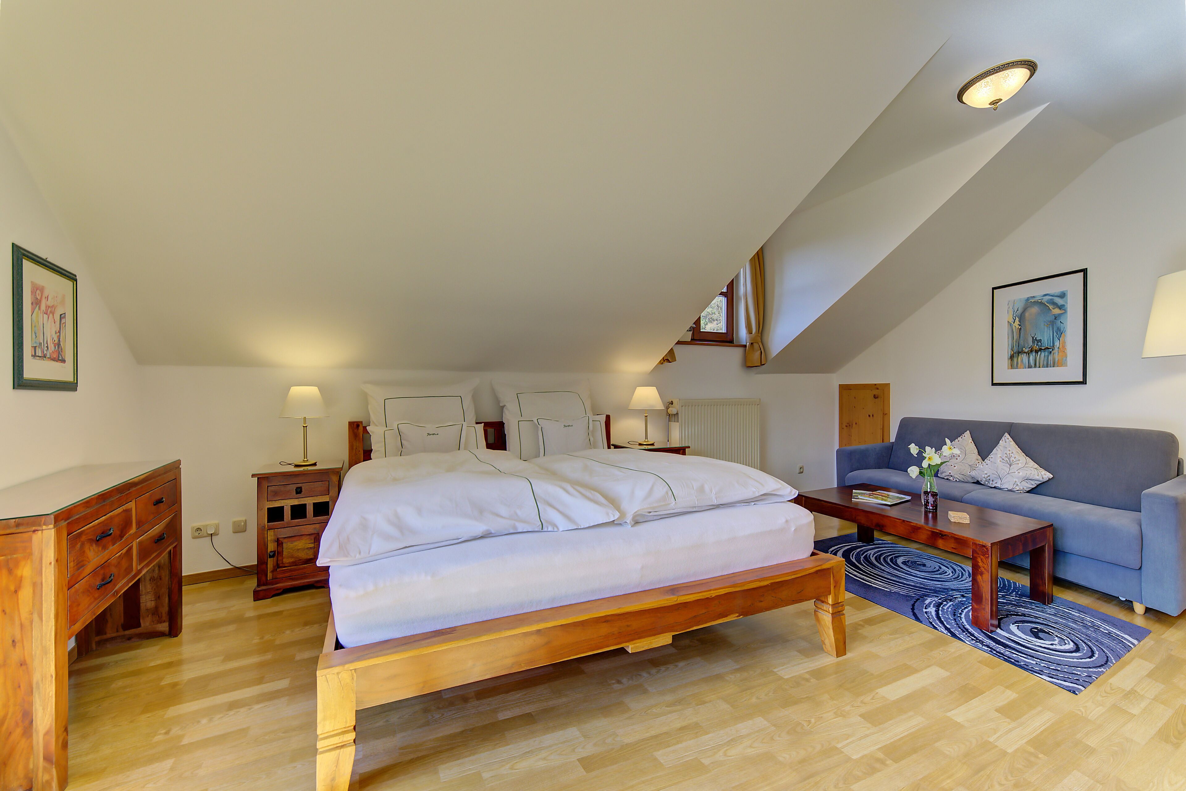 A bedroom with a bed, a wooden nightstand, a blue sofa, a wooden coffee table, and a blue patterned rug.