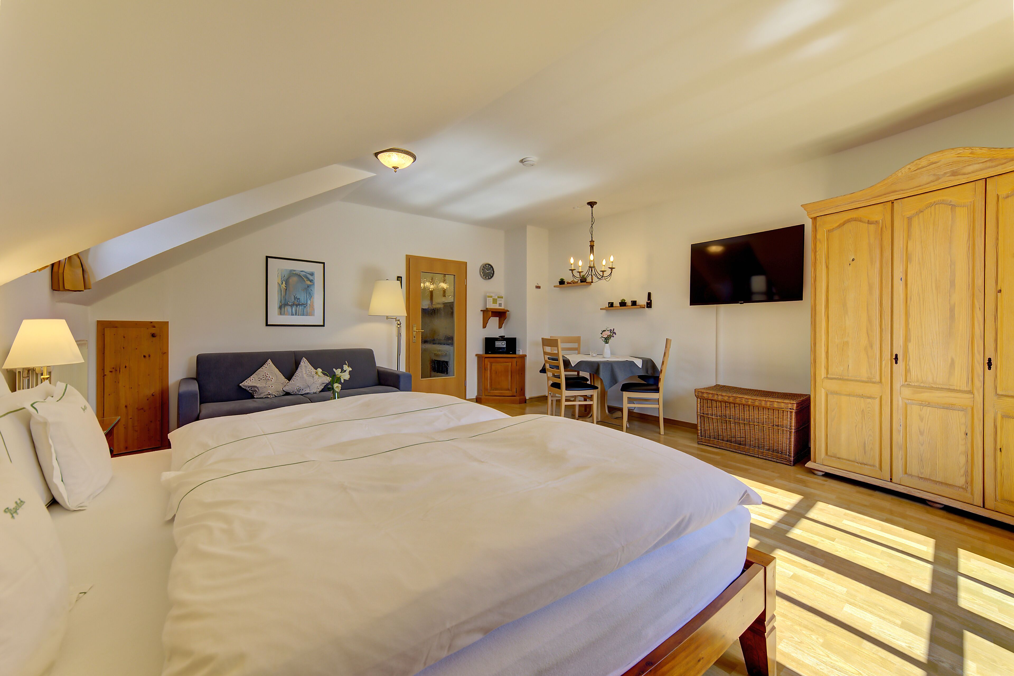 A bedroom with a large bed, a desk, a television, and a wardrobe.