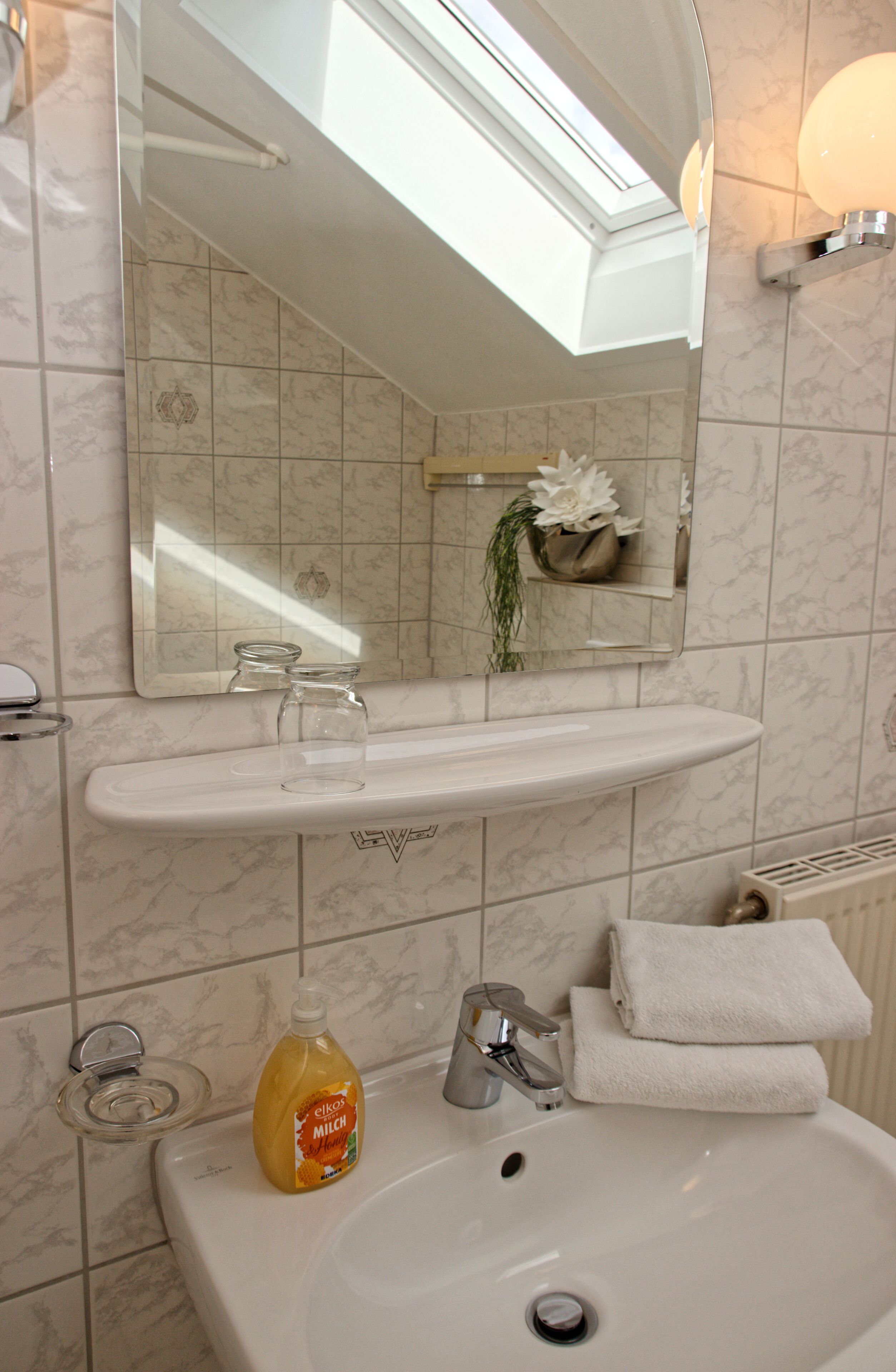 A bathroom with a white sink, a mirror, a towel rack, and a bottle of orange juice.