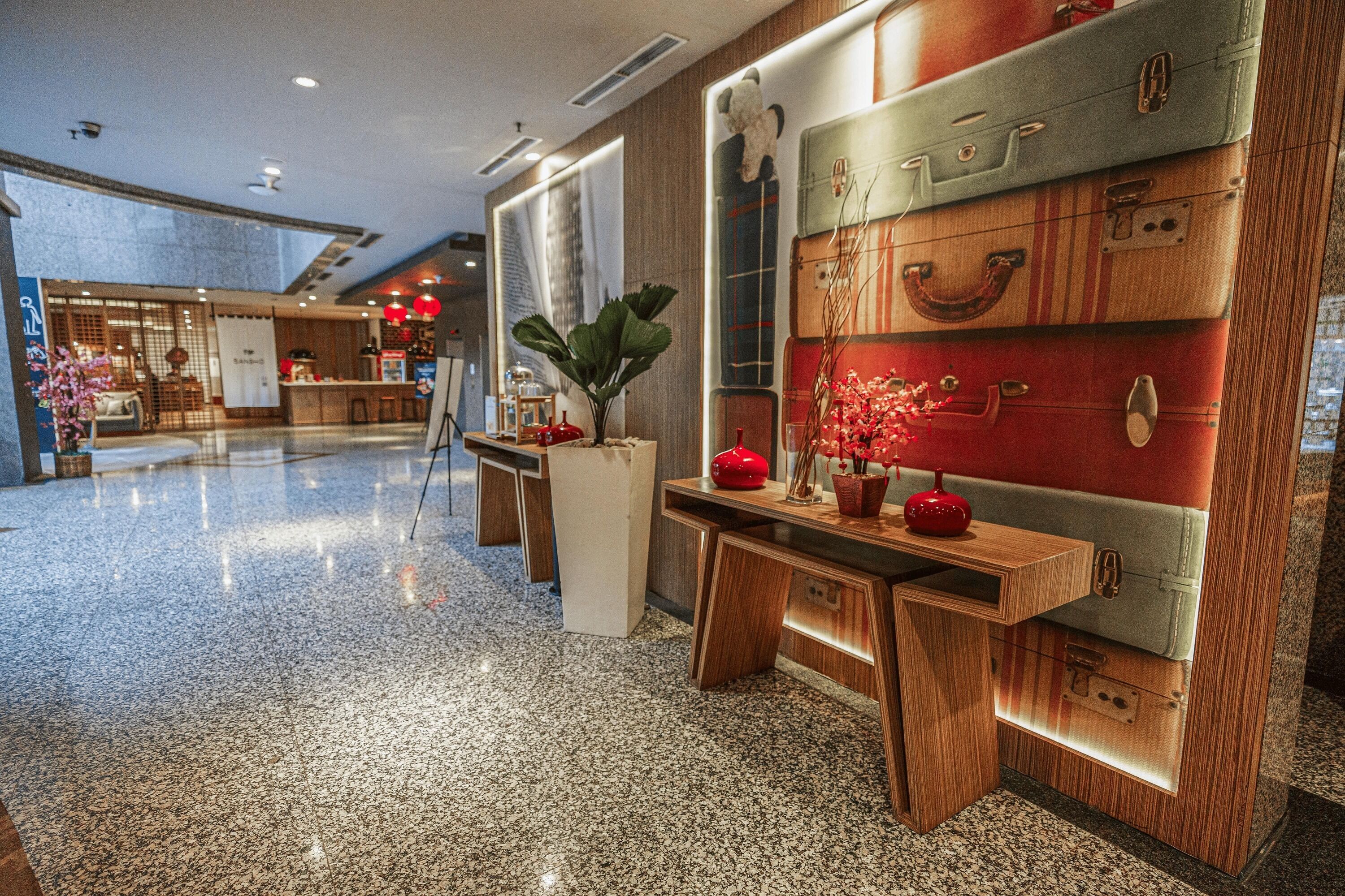 A modern lobby with a polished granite floor, wooden reception desk, and a wall adorned with vintage suitcases.