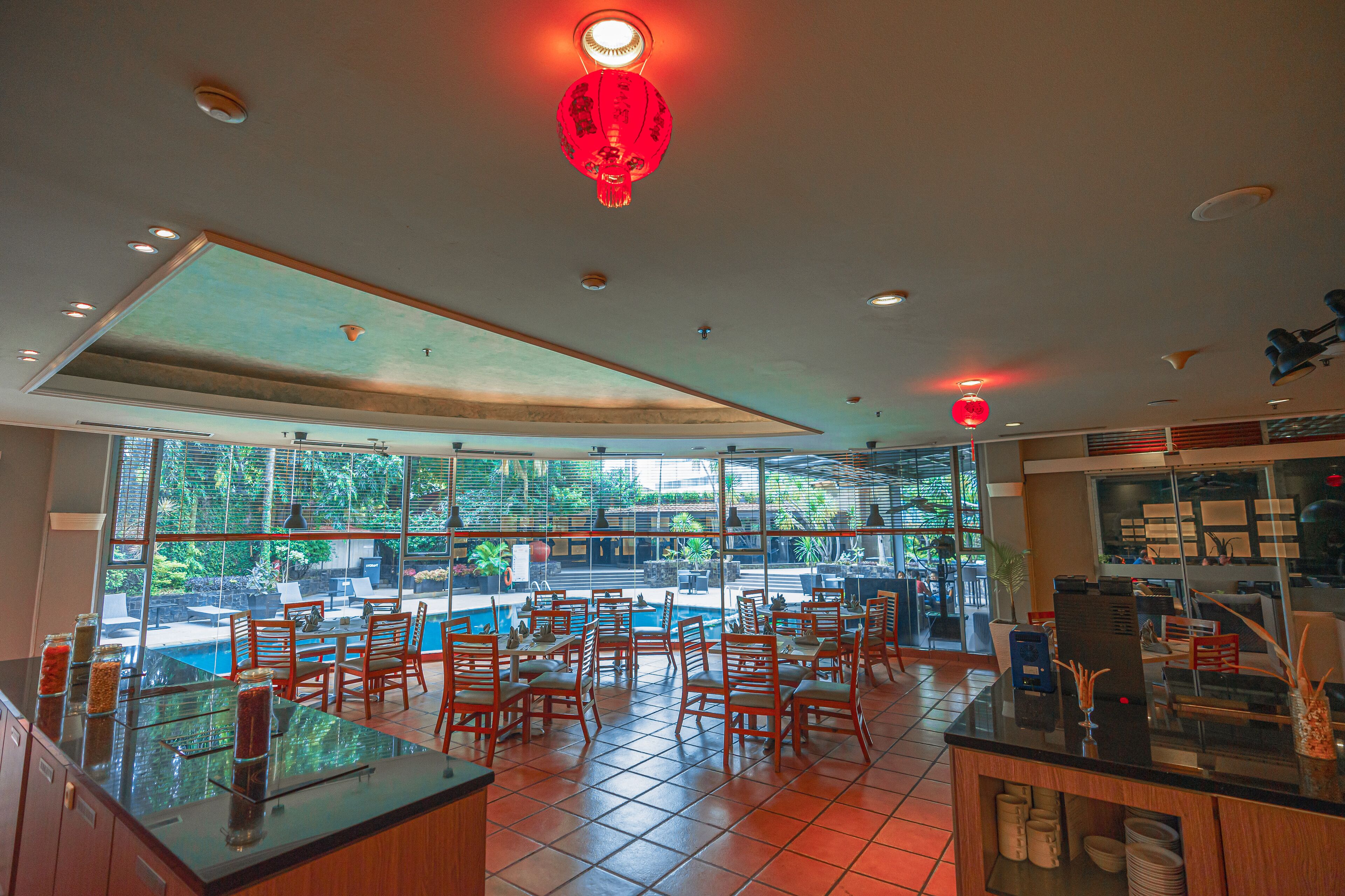 A restaurant with a pool view, wooden chairs, and a red lantern.