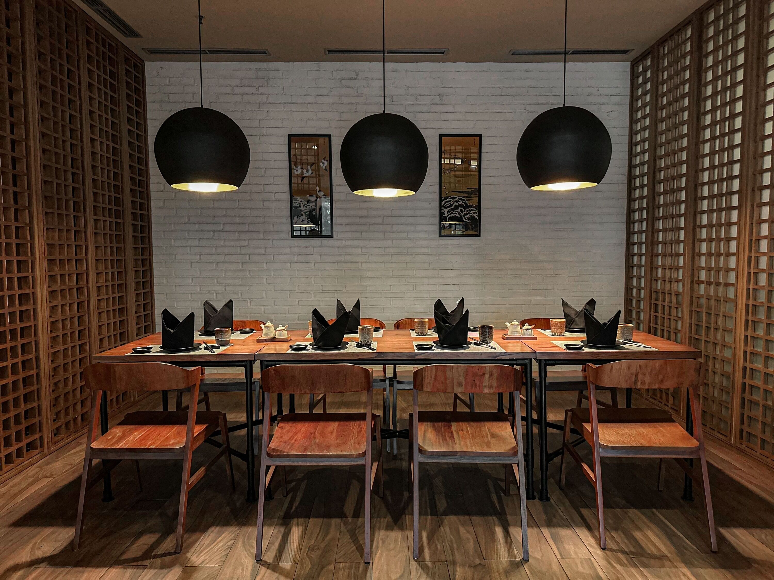 Un espace repas avec une longue table, des chaises et des lampes suspendues.