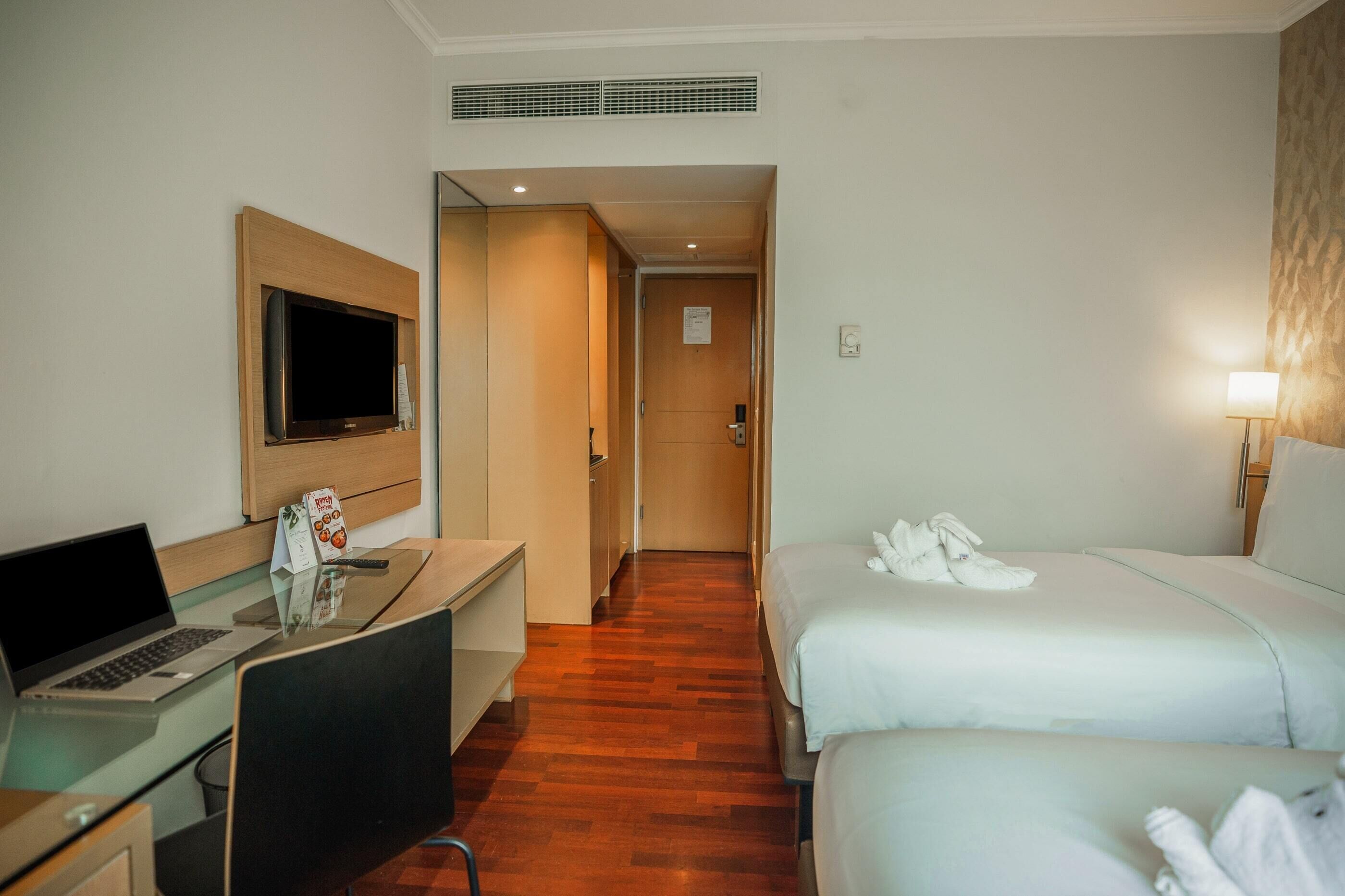 A hotel room with a desk, a television, two beds, and a bathroom door.