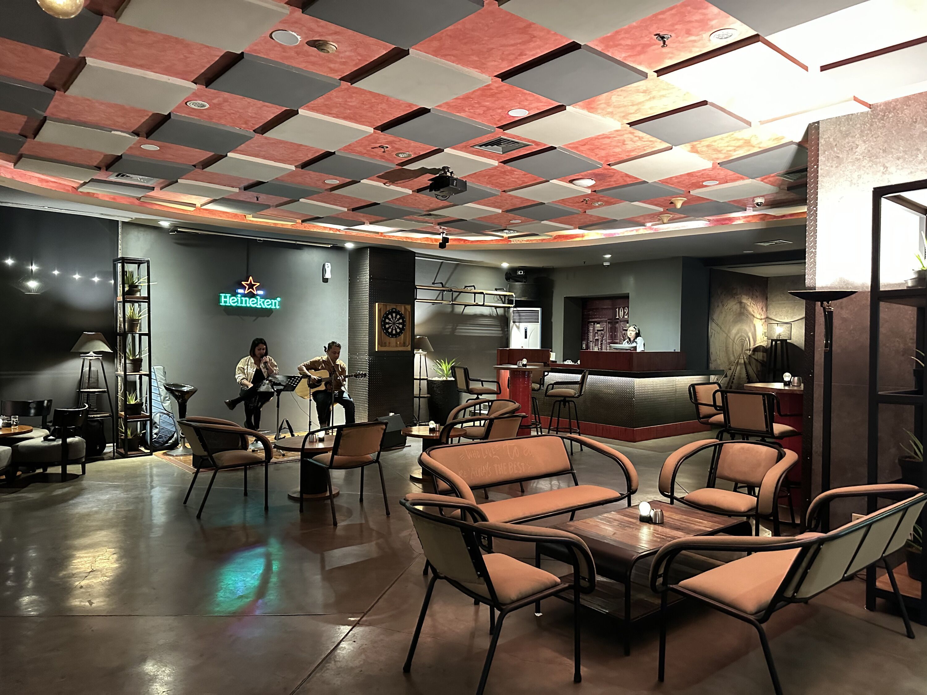 A modern lounge area with a checkered ceiling, seating arrangements, and a bar counter.