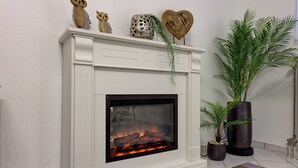 A fireplace with a glass front, decorative items on the mantel, and two potted plants beside it.
