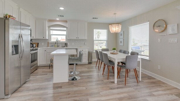 Una cocina moderna con muebles blancos, un refrigerador de acero inoxidable y un comedor con mesa blanca y sillas grises.